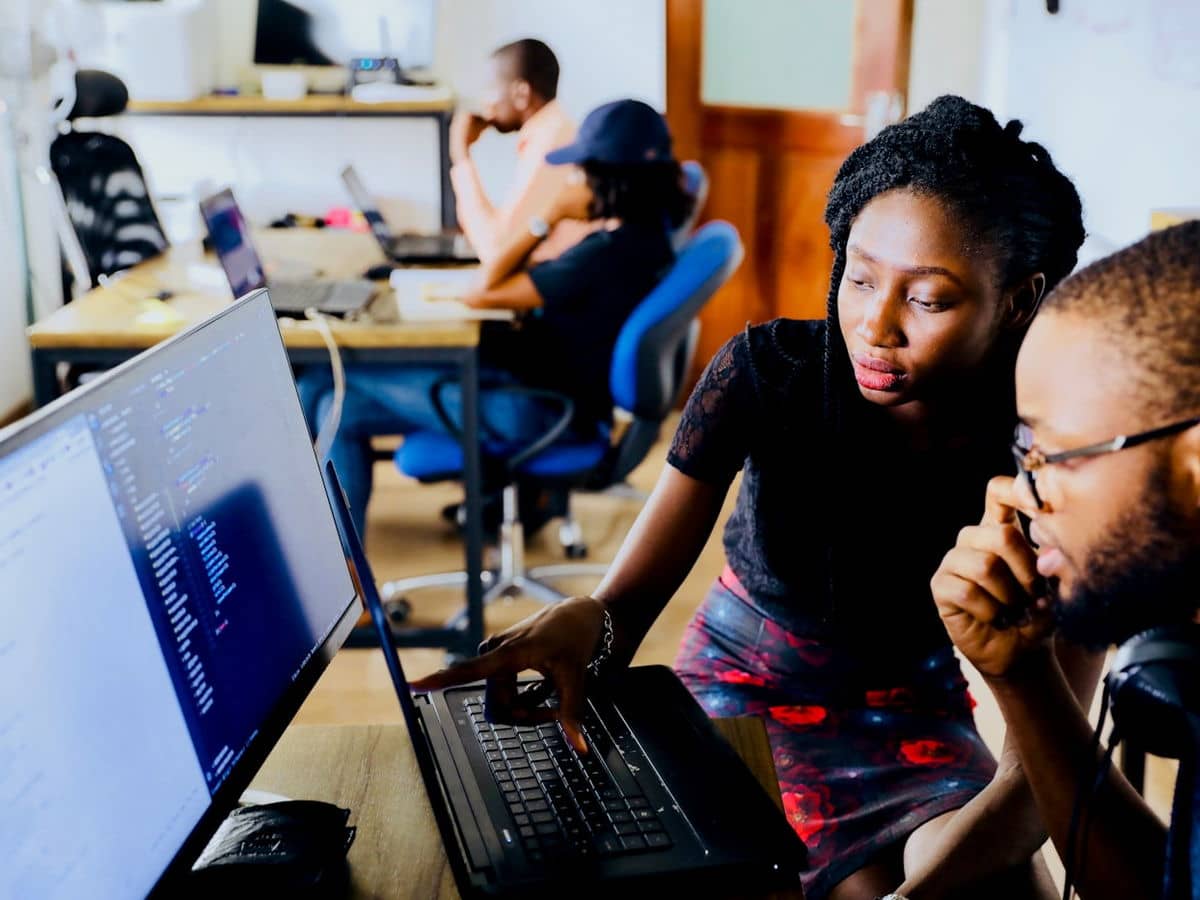 Dois profissionais de tecnologia trabalhando juntos em frente a monitores
